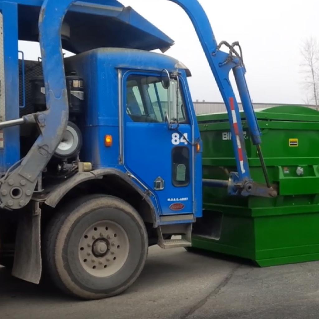 Truck collecting industrial waste bins for routine disposal service